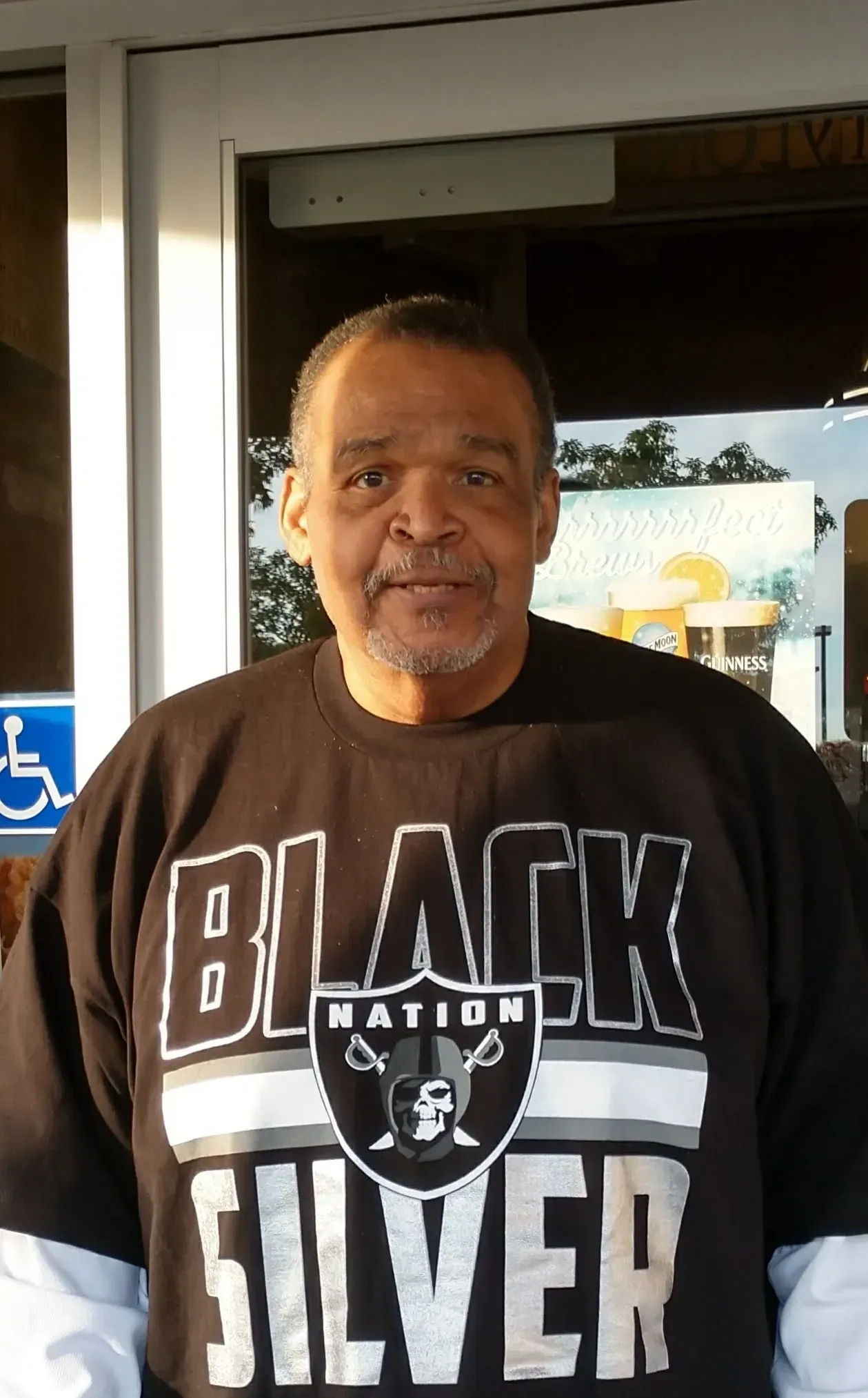 Man wearing a black Raiders shirt, standing in front of a door.