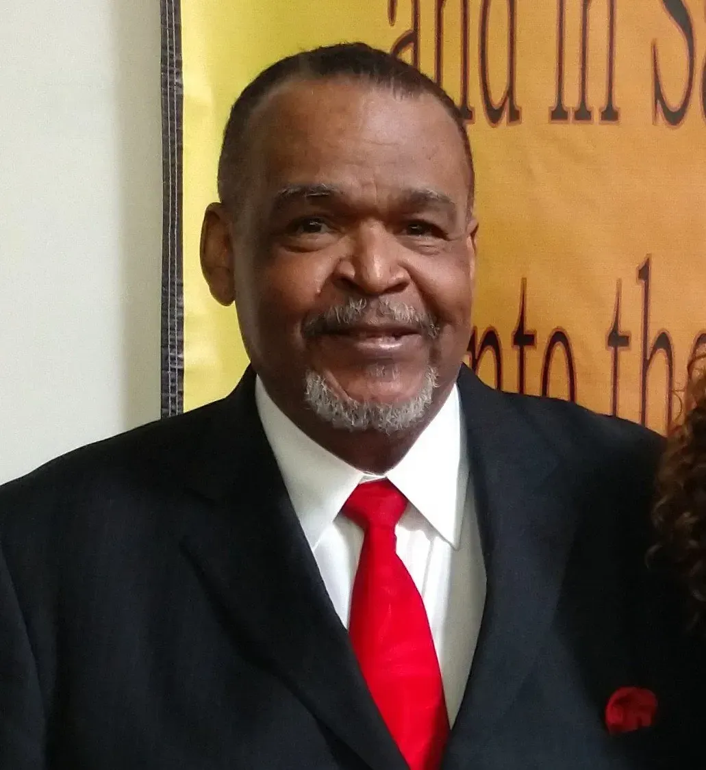 Man in black suit, red tie, smiling at camera. 