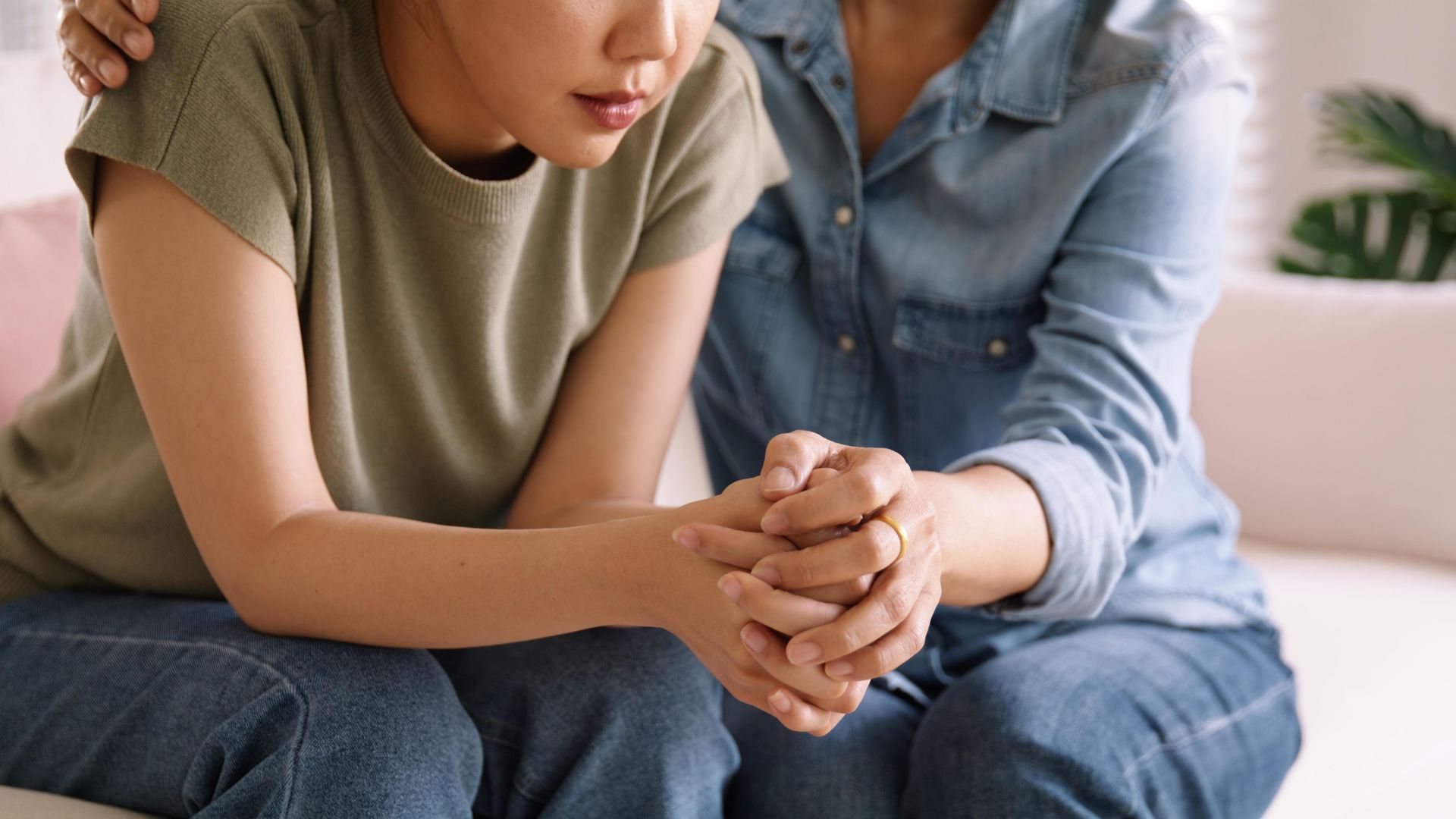 Woman being comforted by another, hands clasped, indoors.