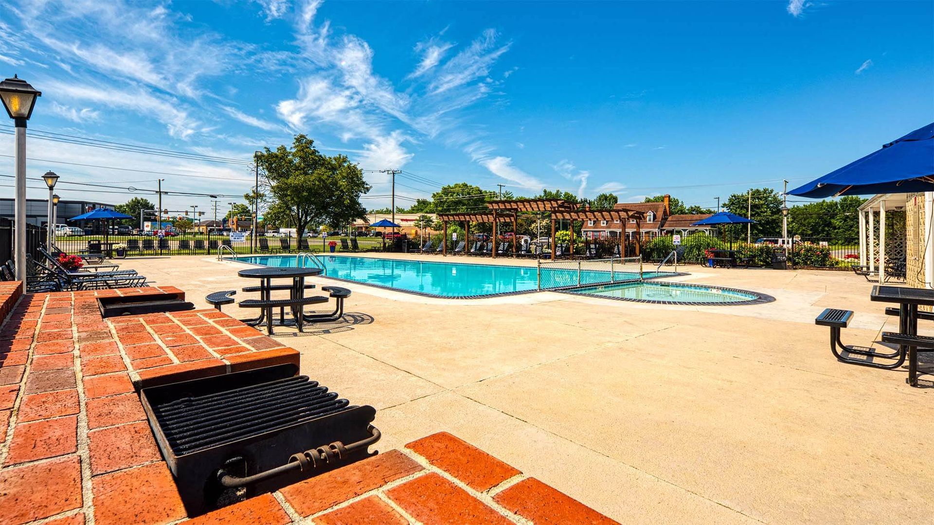 Outdoor apartment community pool with lounge chairs, tables, umbrellas, and a pergola.