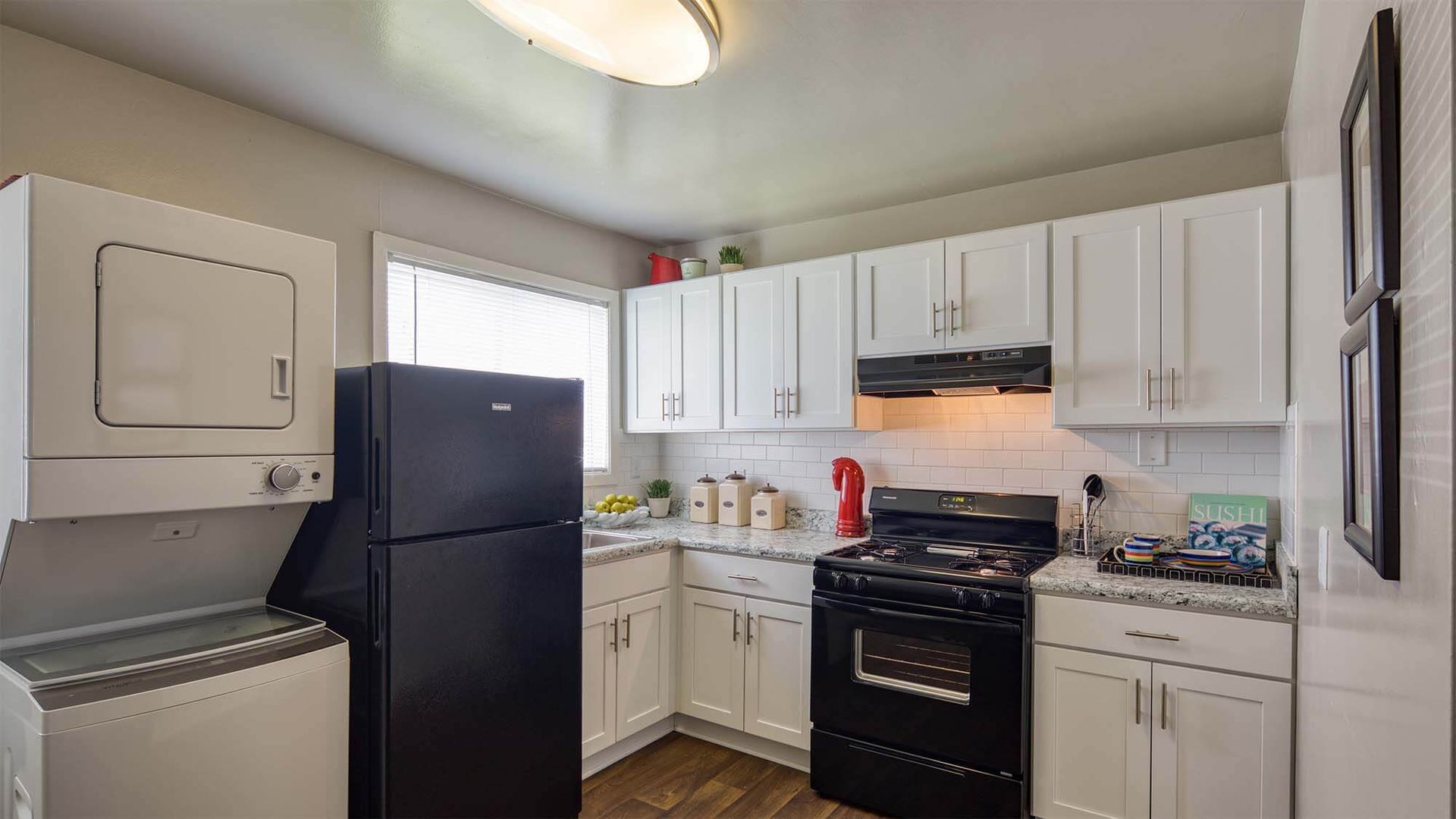 Kitchen with white cabinets, black fridge and stove, and a stacked washer/dryer on the left.