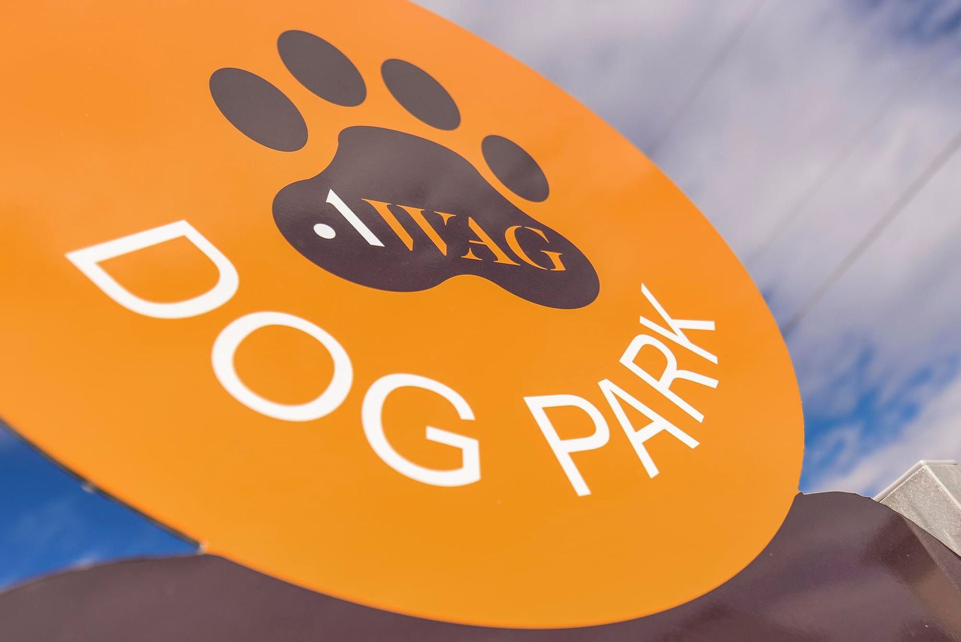 Orange circular sign with a black paw print and DOG PARK lettering.