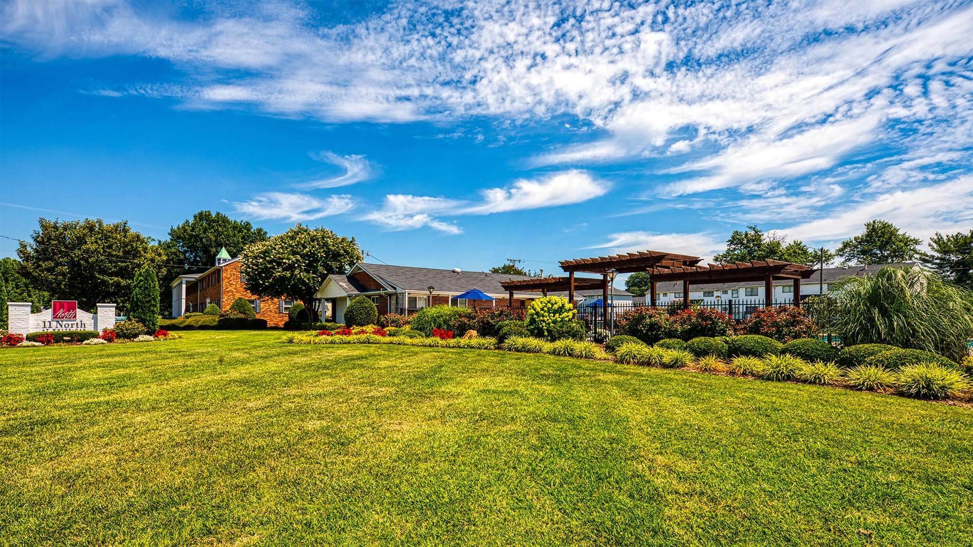 Wide exterior view of a landscaped multifamily community with a pergola and campus buildings.