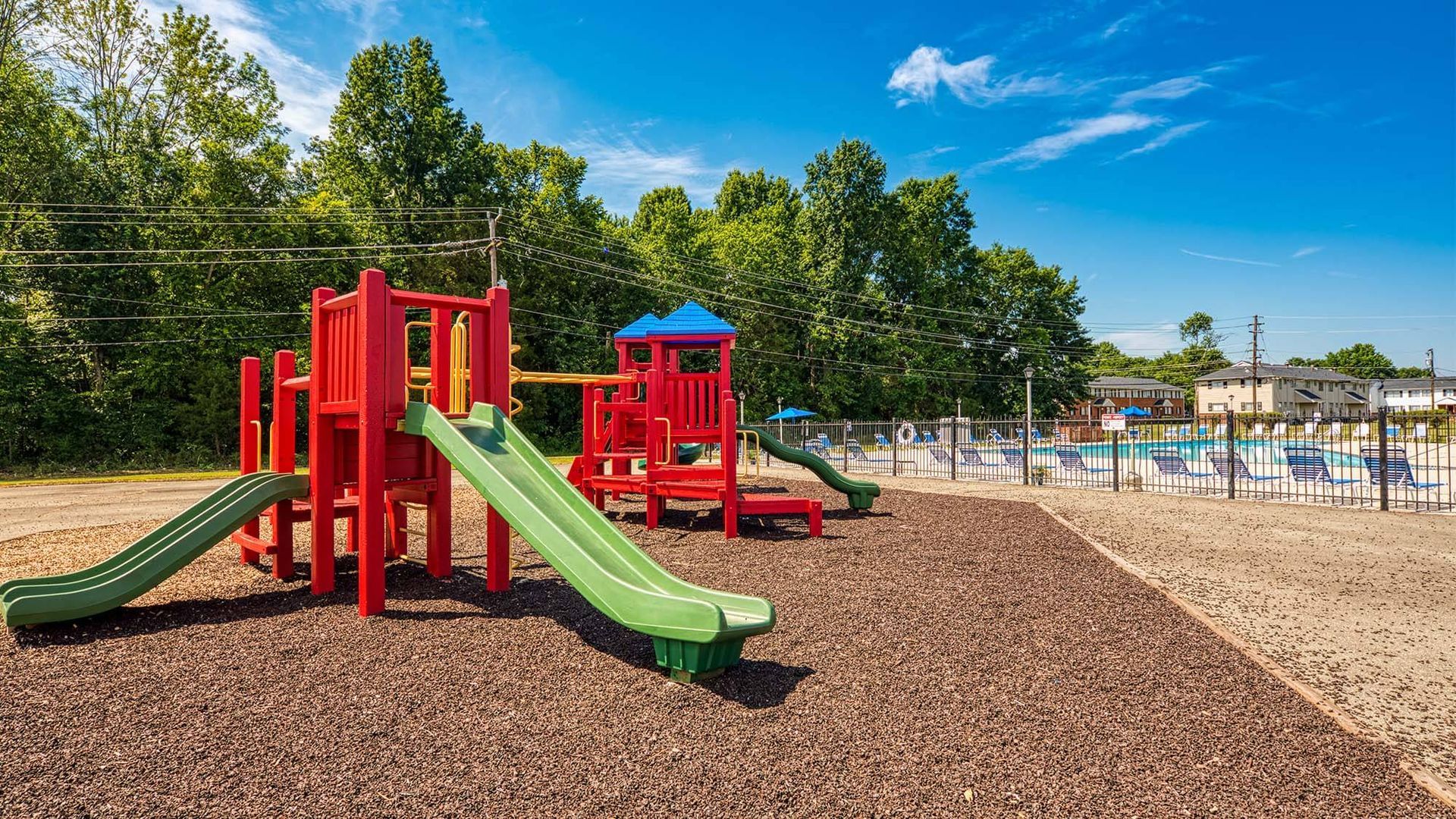 Playground with red and green equipment near a pool at an apartment community.