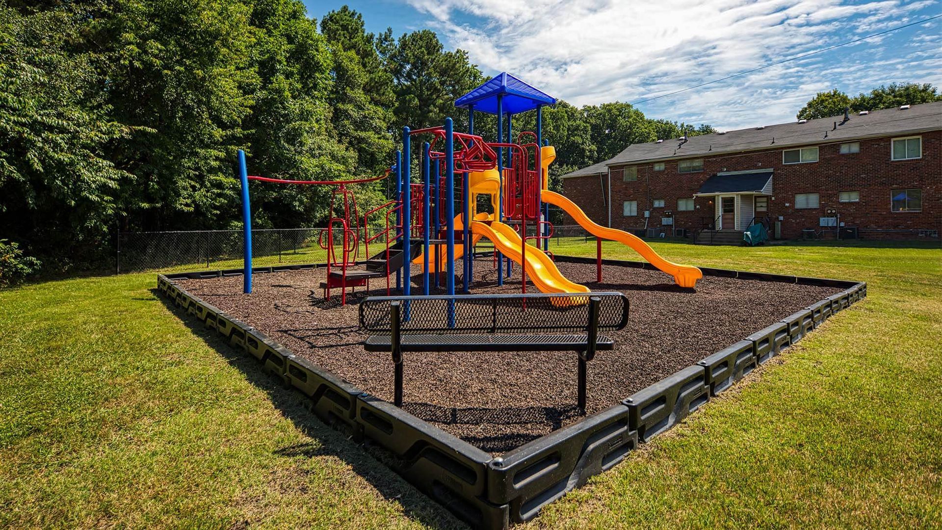 Colorful playground with slides and climbing structures in a fenced area beside a brick apartment building.