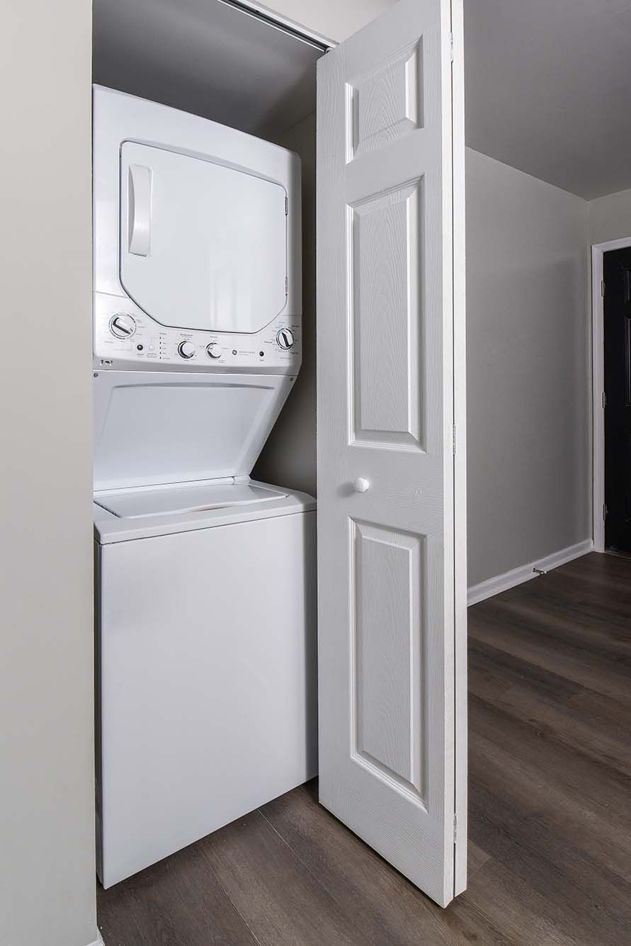 White stacked washer and dryer in a closet behind a partially open door.