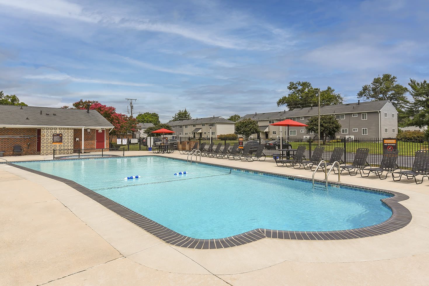 Outdoor community swimming pool with lounge chairs and red umbrellas at an apartment complex.