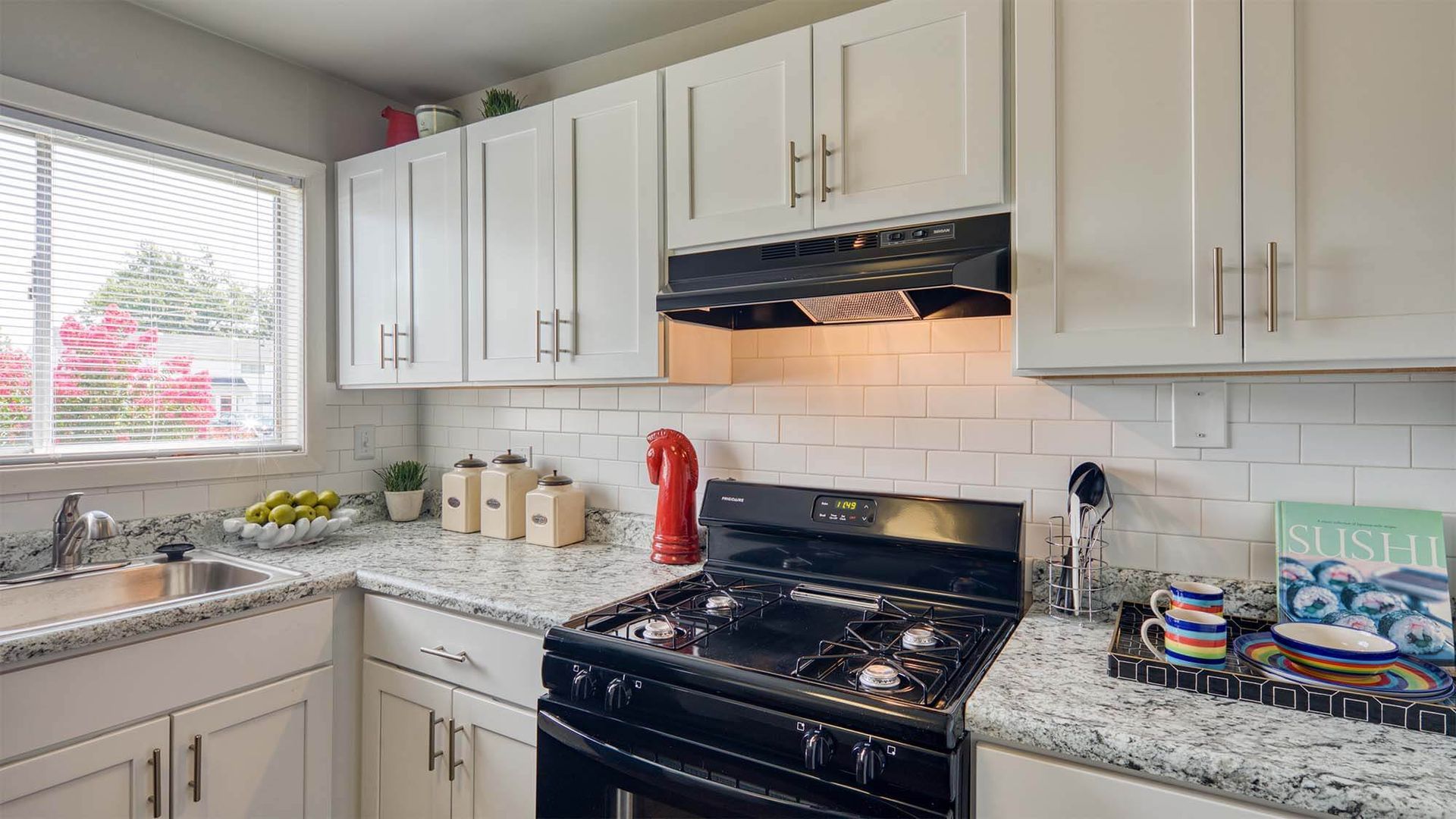 Bright kitchen with white cabinets, granite countertops, stainless-steel stove and range hood, and a window.
