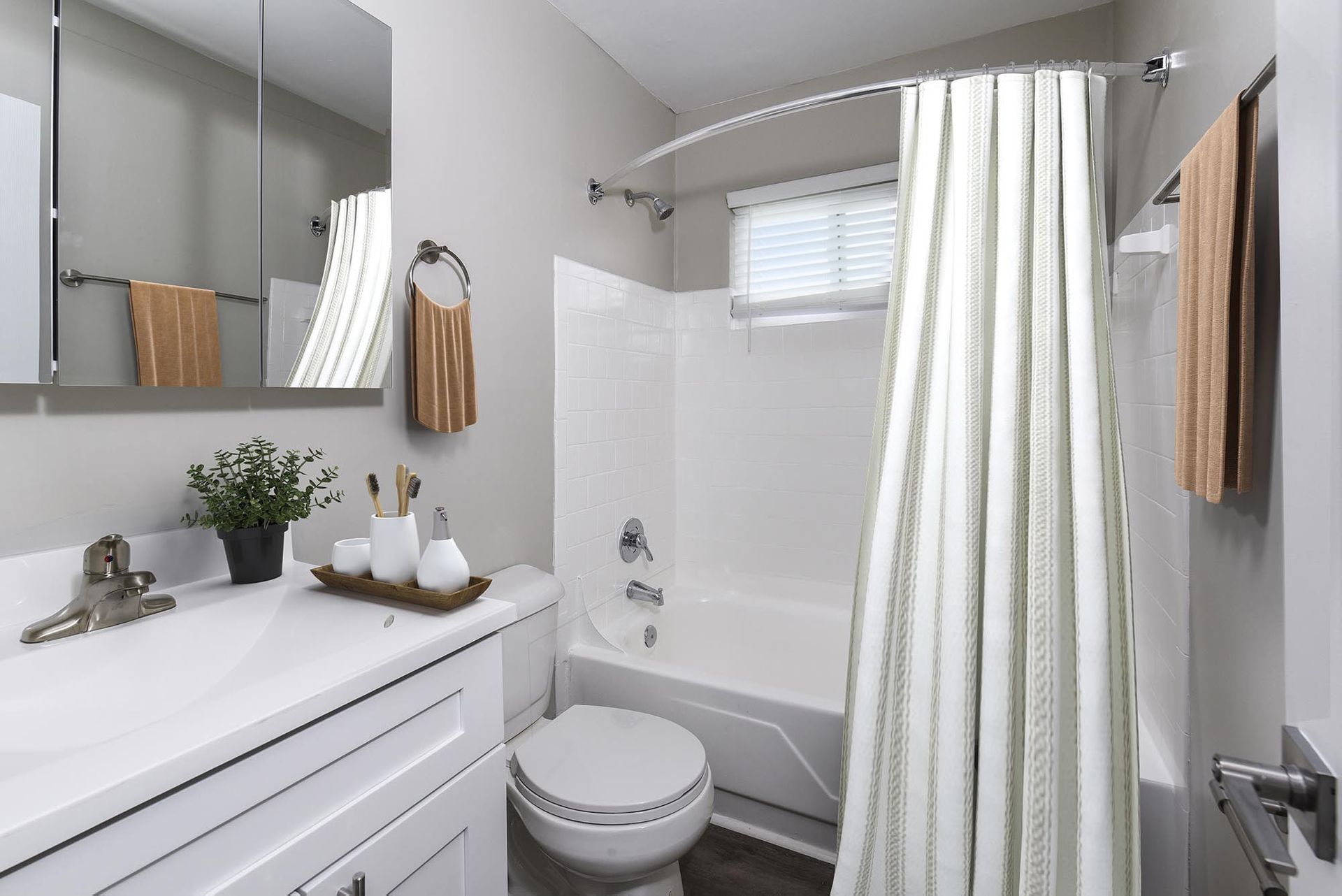 White apartment bathroom with vanity, mirrored cabinet, toilet, and a tub/shower combo.