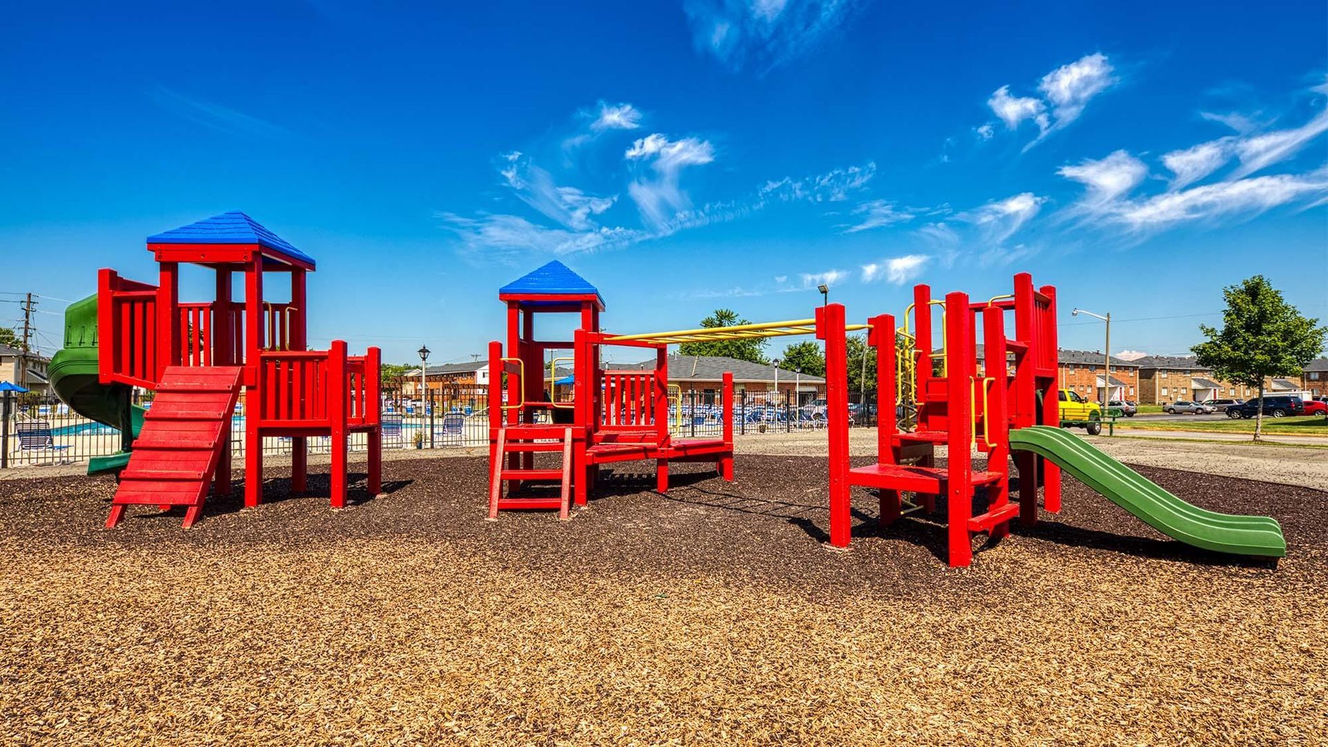 Colorful outdoor playground with red structures, a green slide, and blue sky.