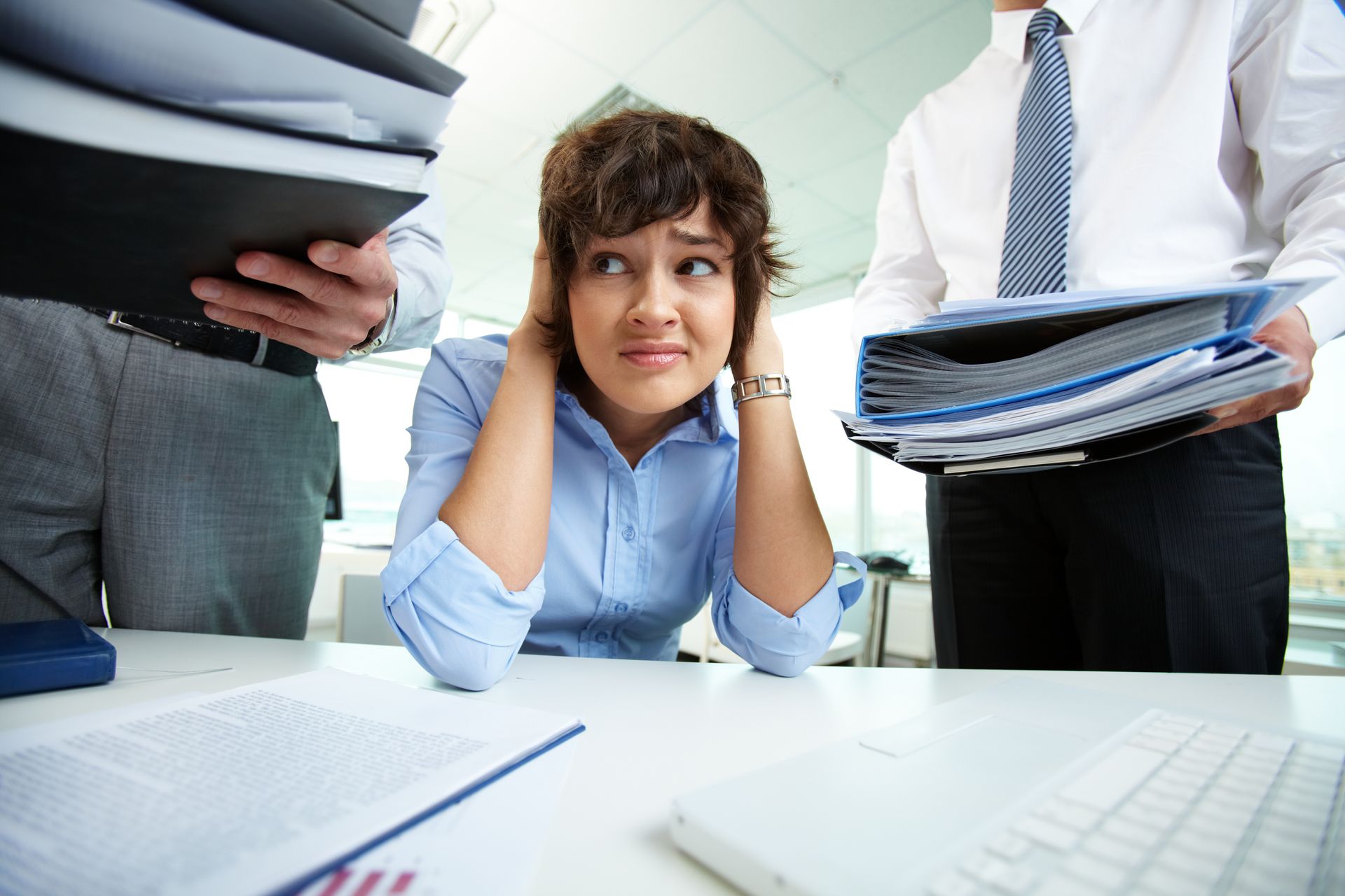 A woman sits at a desk with her hands covering her ears