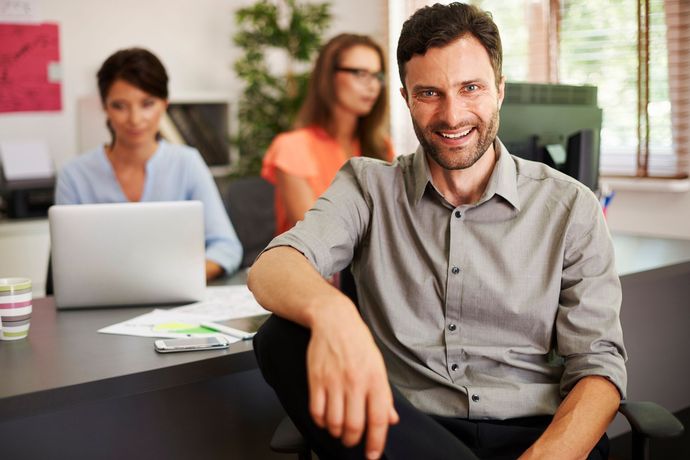 Um homem está sentado em uma mesa na frente de um grupo de pessoas.