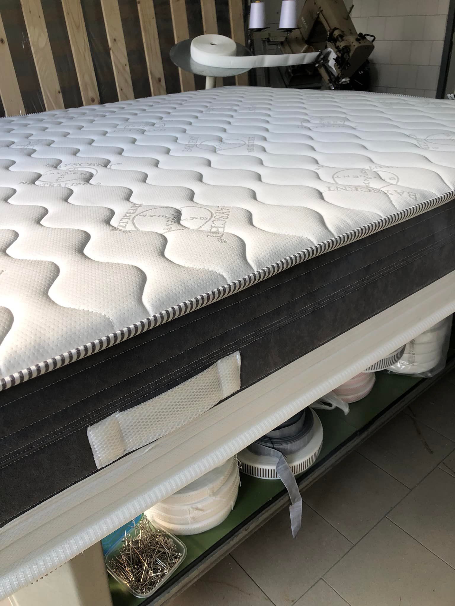 Primo piano di un materasso parzialmente assemblato con parte superiore trapuntata bianca e pannello laterale grigio scuro in un'officina.