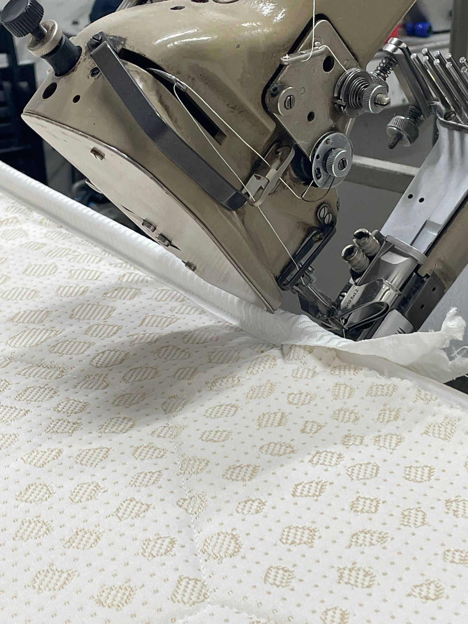 Una macchina per cucire il bordo del nastro del materasso che lega il bordo del tessuto di un pannello di materasso bianco decorato.