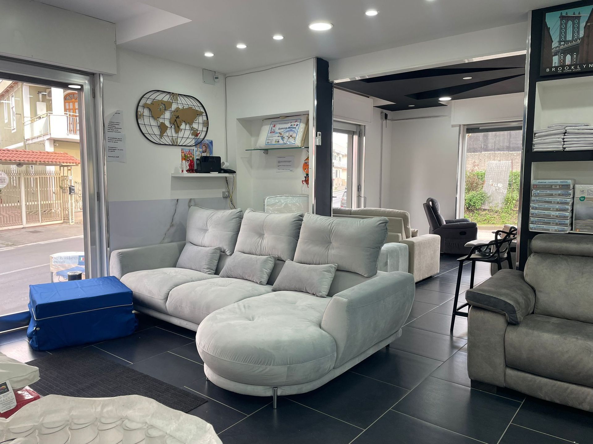 Un divano componibile di colore chiaro nello showroom di un negozio di mobili con un pouf blu in primo piano e una poltrona reclinabile nelle vicinanze.