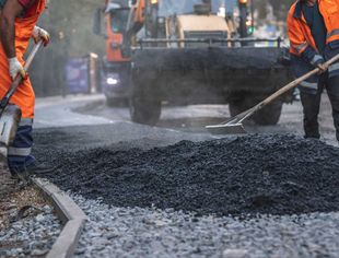 Road construction worker leveling asphalt with a shovel.