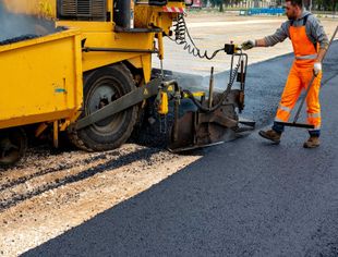 Machine operator to spread asphalt, intervenes on the control panel to adjust the asphalt paving 
