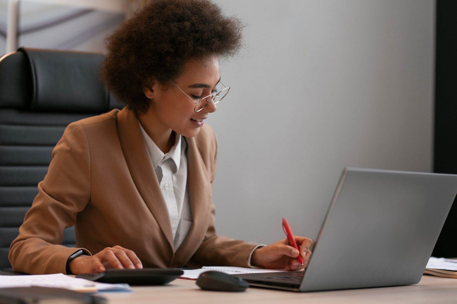 Woman in tan blazer, working at a laptop