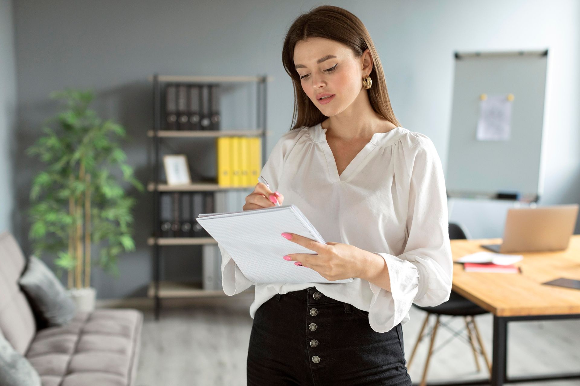Woman in white blouse and black pants, looking at documents in an office setting.