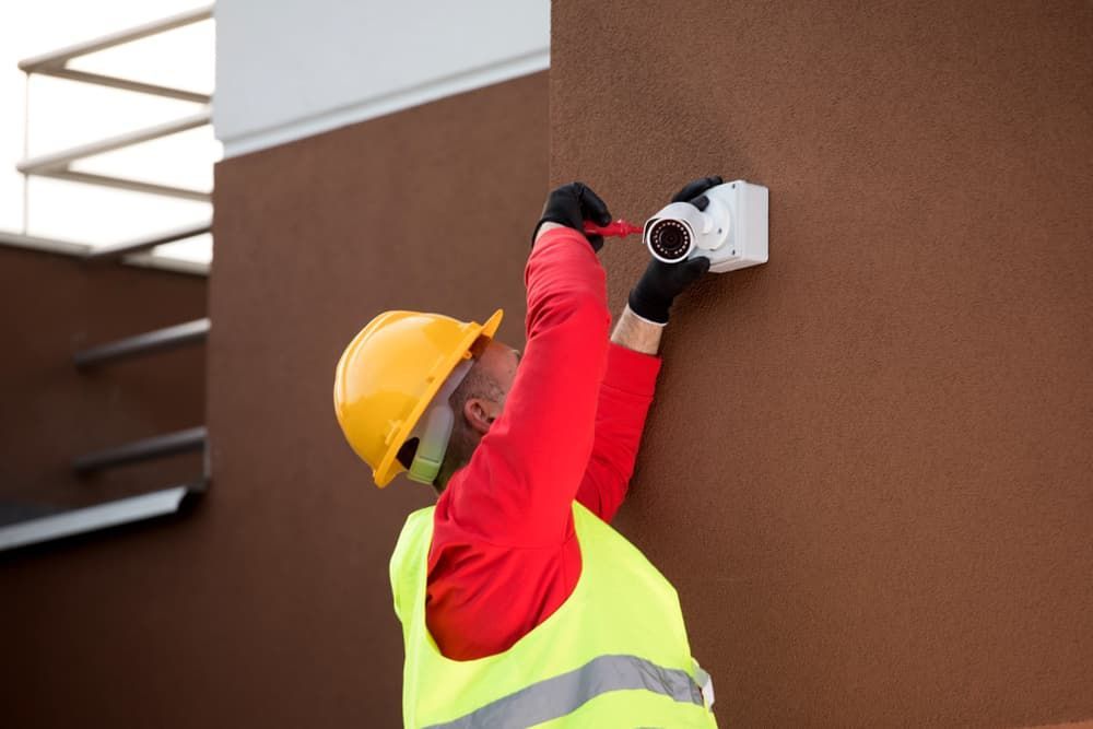 A Man is Installing a Security Camera on the Side of a Building — SEP Electrical Pty Ltd in Kiama, NSW