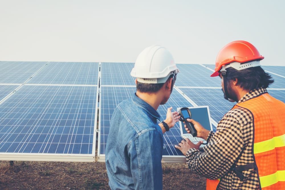 Two Men Are Looking at a Tablet in Front of a Solar Panel — SEP Electrical Pty Ltd in Towradgi, NSW