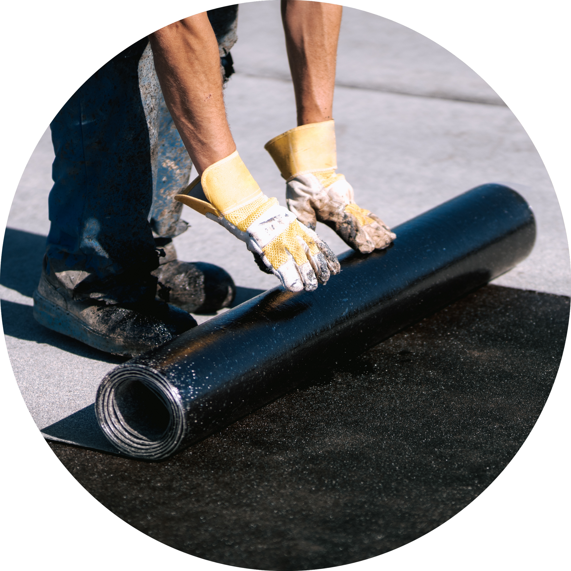 A man wearing gloves is laying a roll of asphalt on the ground.