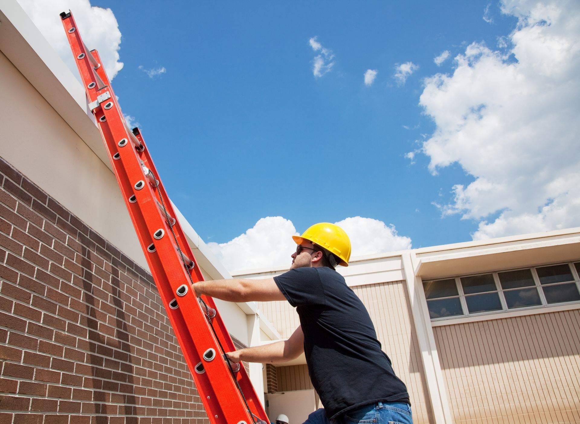 A man wearing a hard hat is climbing a red ladder.