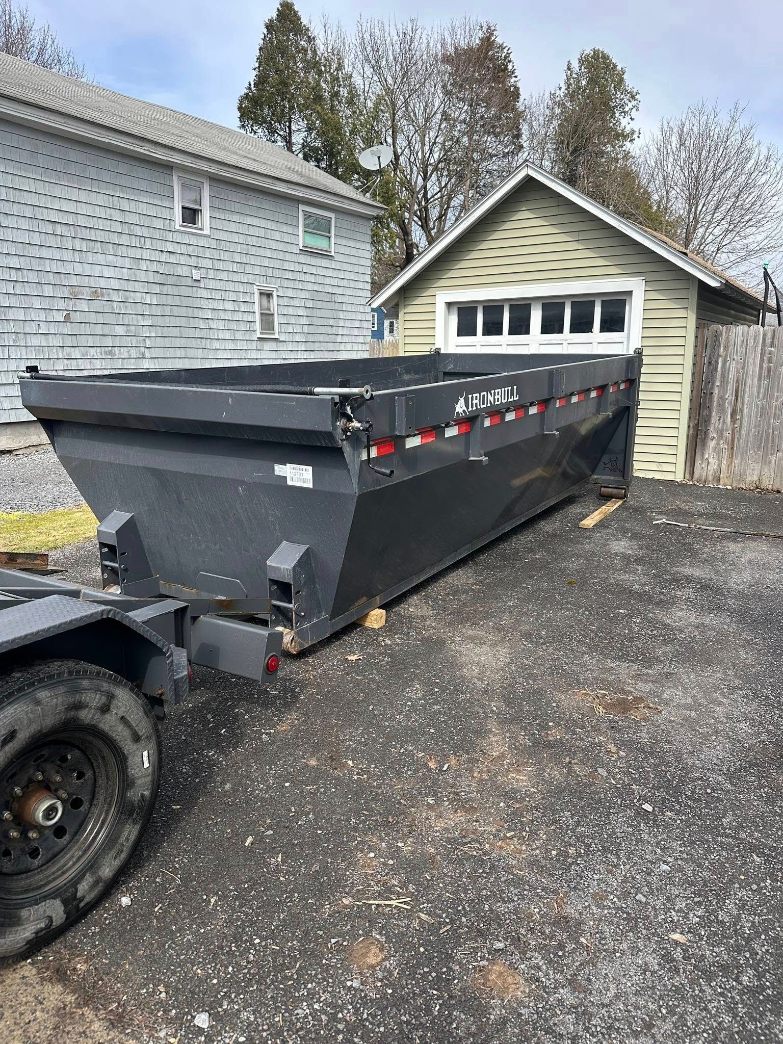A dumpster is sitting on top of a trailer in front of a house.