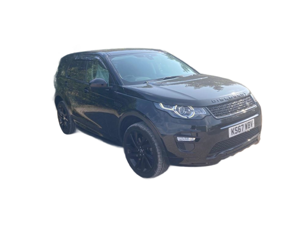 Black Land Rover Discovery Sport parked on a gravel surface with trees in the background.