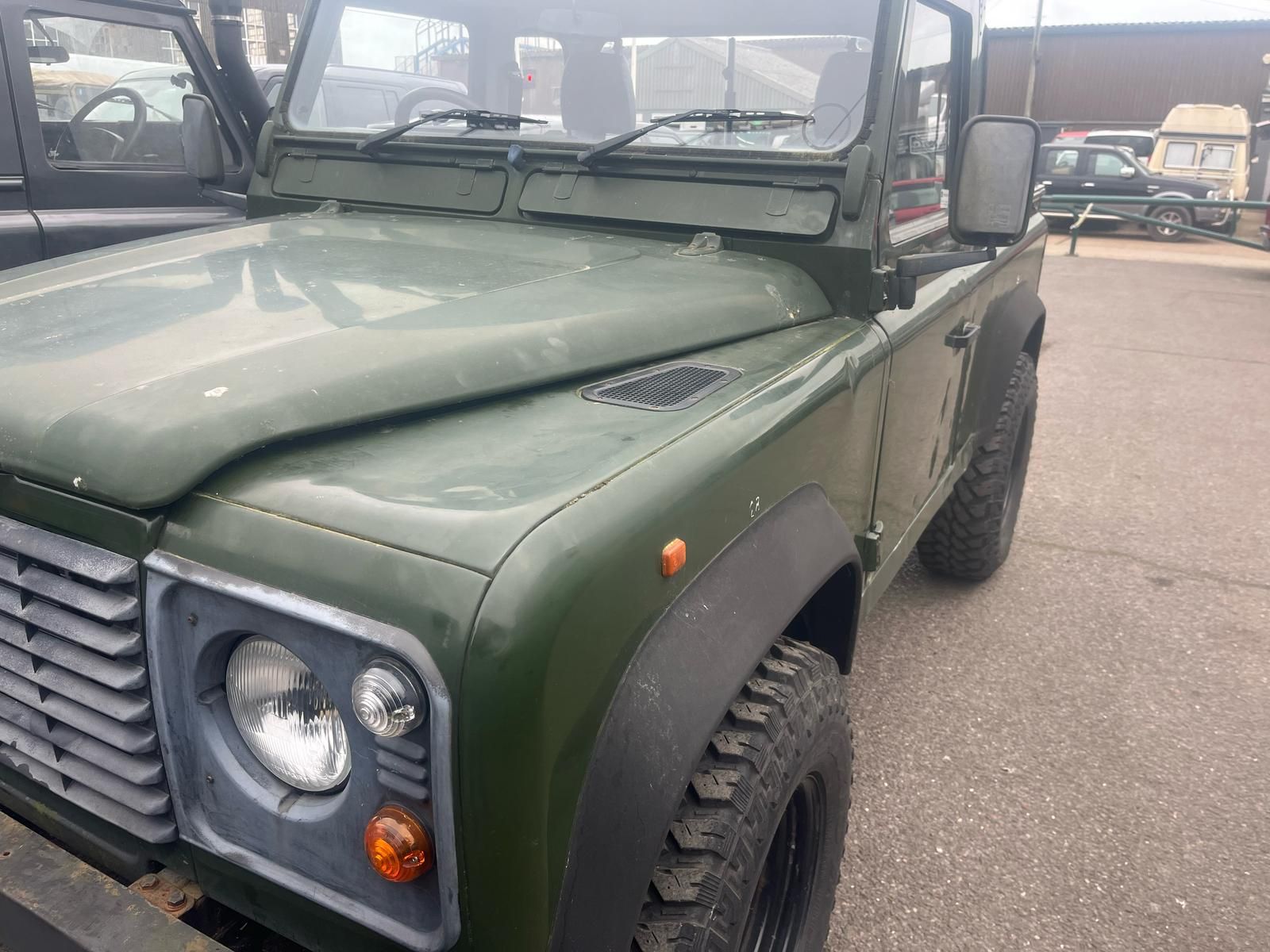 Green Land Rover Defender with black wheels and fender flares parked outdoors.