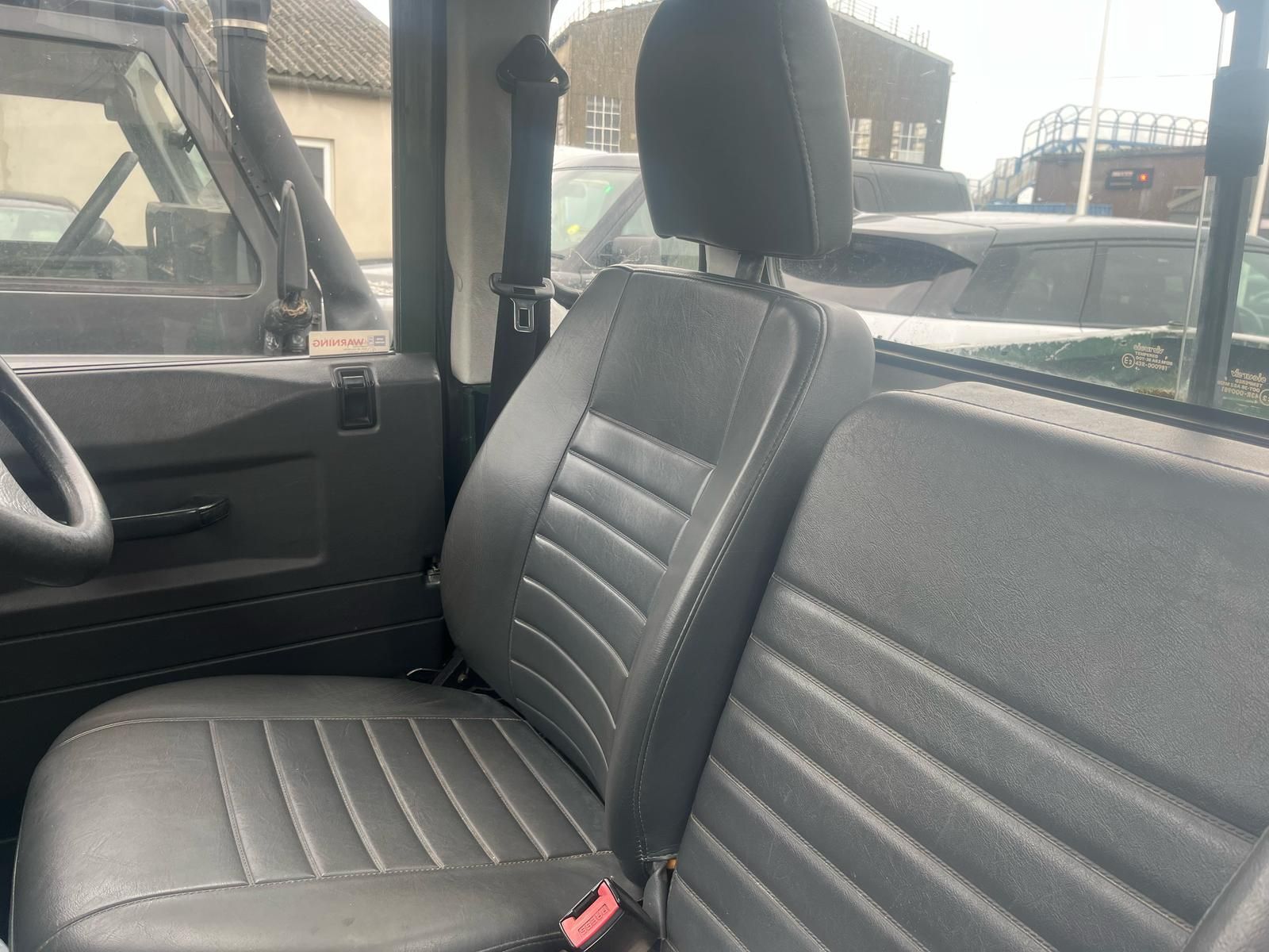 Interior of a dark gray Land Rover Defender, showing the driver's seat, passenger seat, and partially visible dashboard and steering wheel.