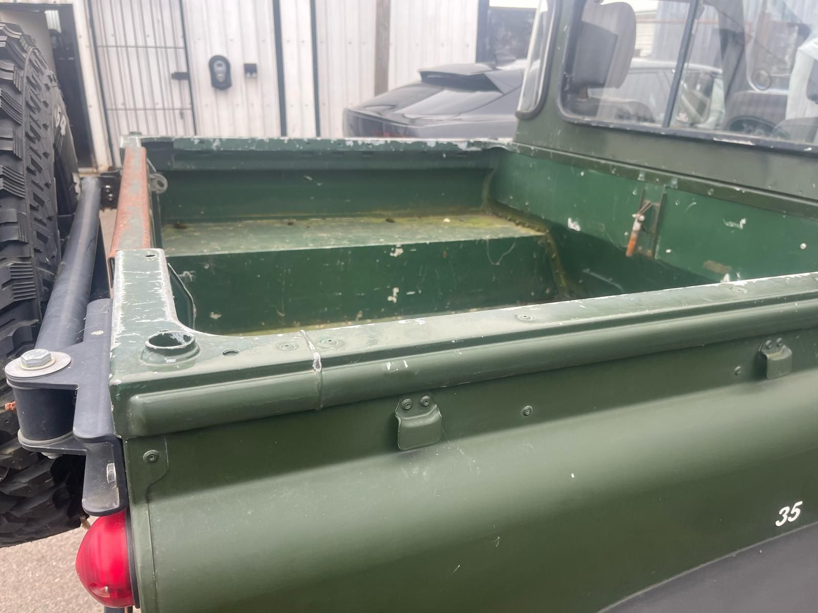 Close-up of the rear of a green pickup truck bed with a spare tire mounted. The bed has a step-down and some wear.