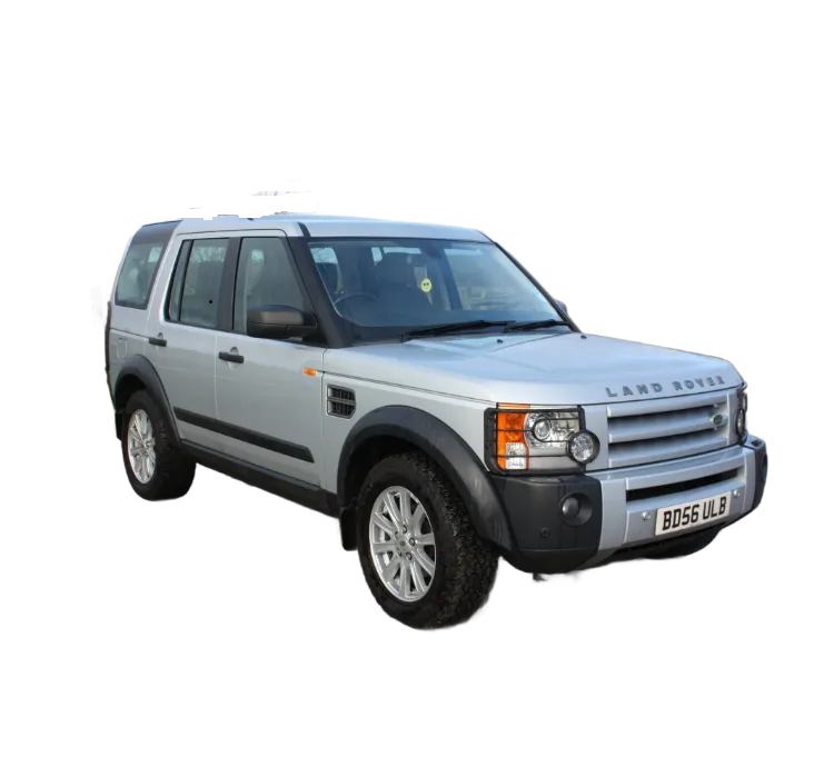 Silver Land Rover Discovery SUV parked on a paved surface in front of a wooden fence and field under a cloudy sky.