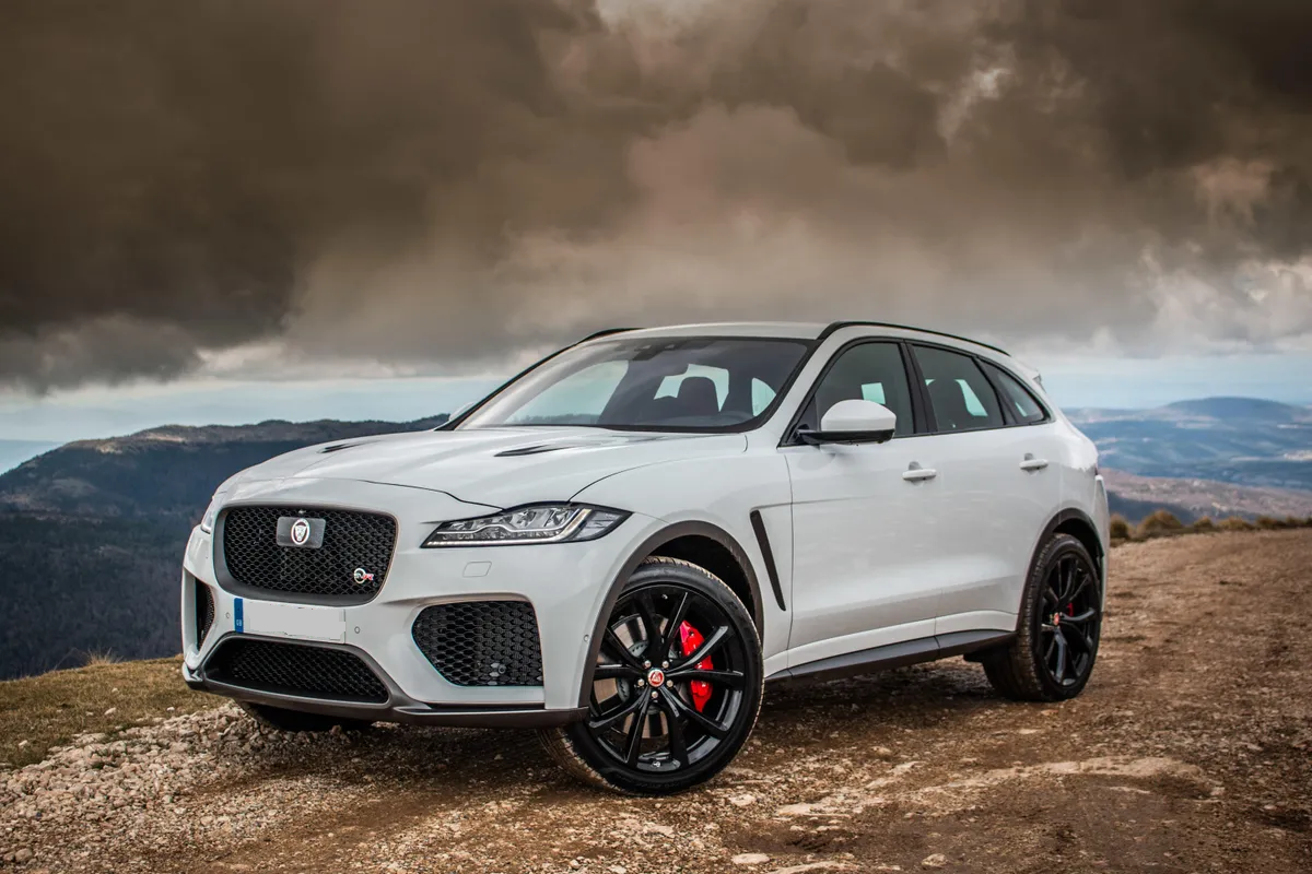 Green Land Rover Defender parked in a desert landscape. A person stands on the roof, overlooking the scenery.