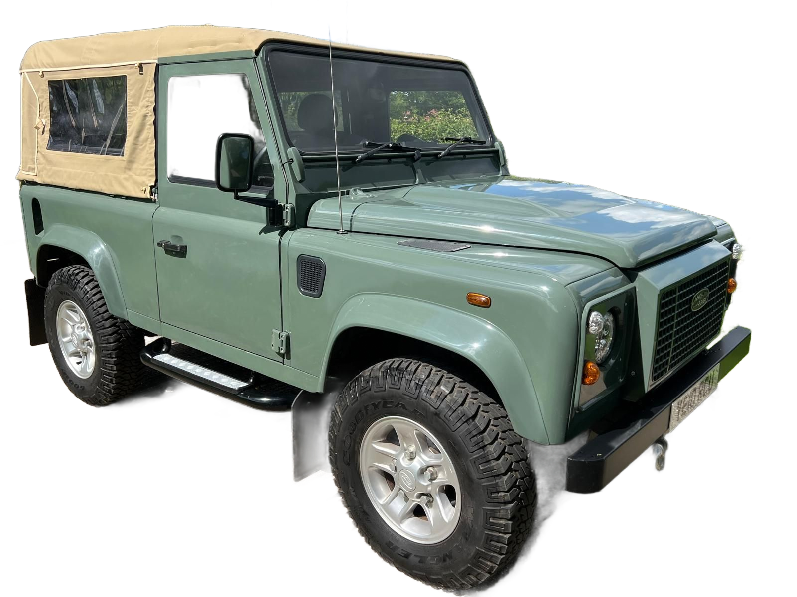 White Land Rover driving through a snowy forest road; headlights on, snow chains on tires.