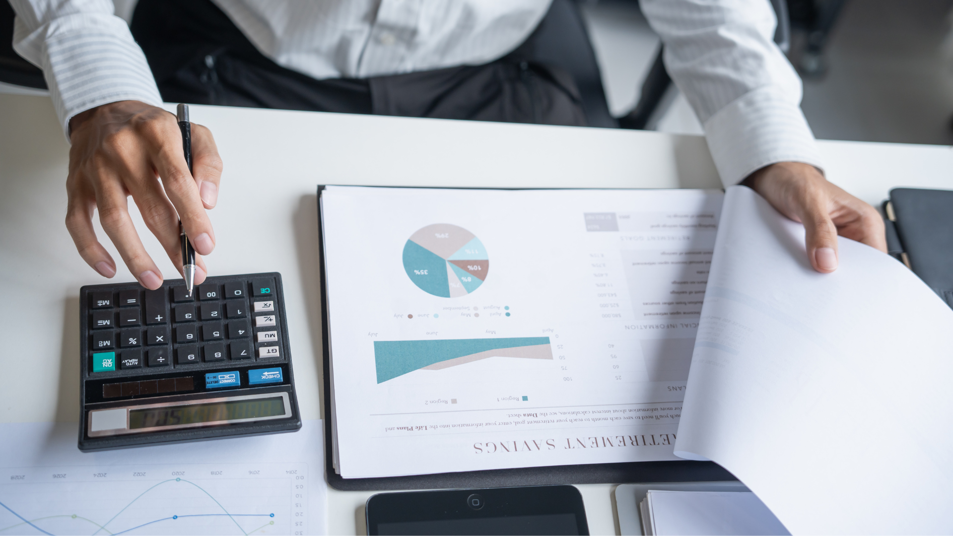 A man sitting at an office desk, working on financial figures. With data sheets and calculator.