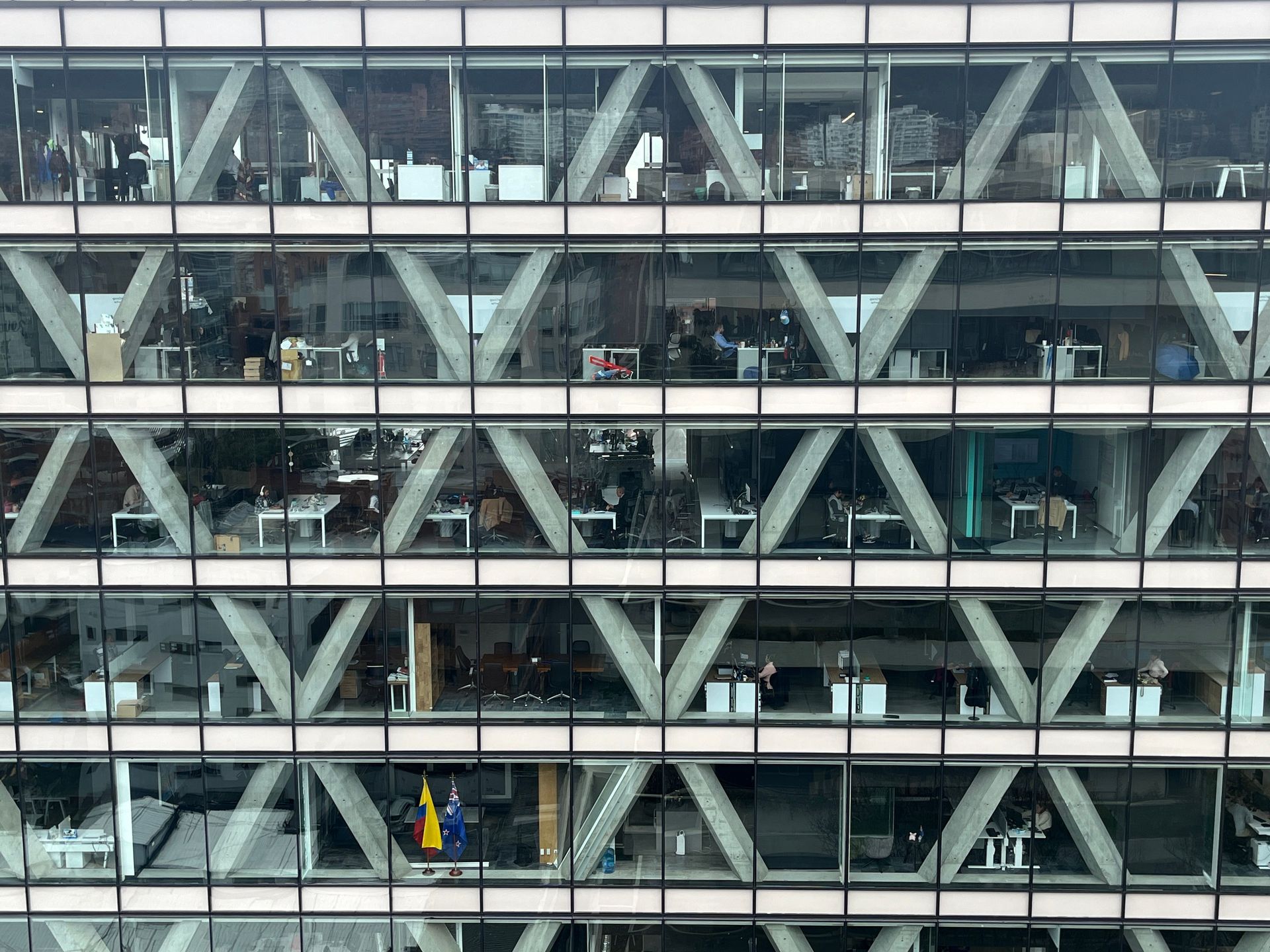 Glass-fronted office building with crisscross steel beams and people visible on multiple floors