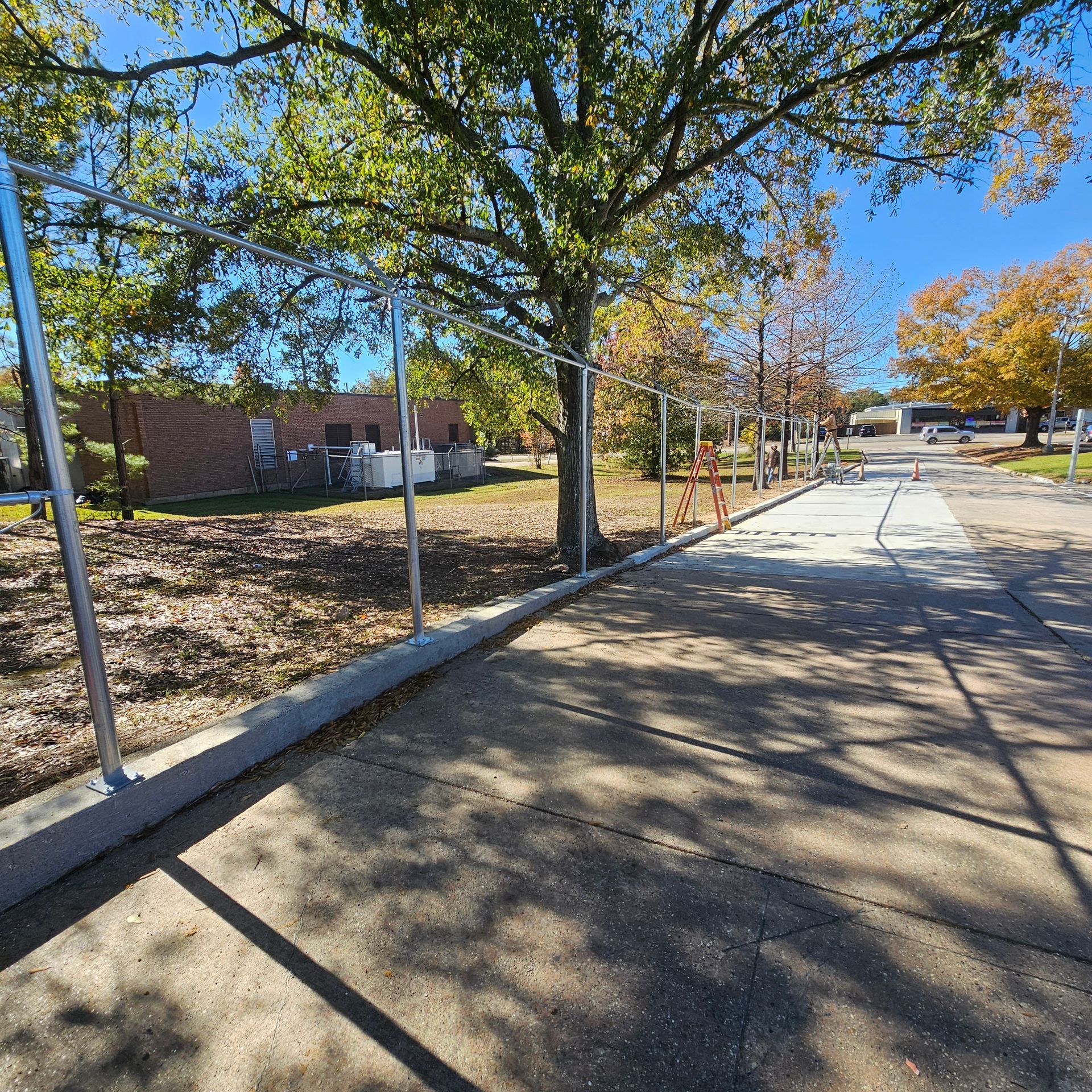 A sidewalk with a fence and trees in the background