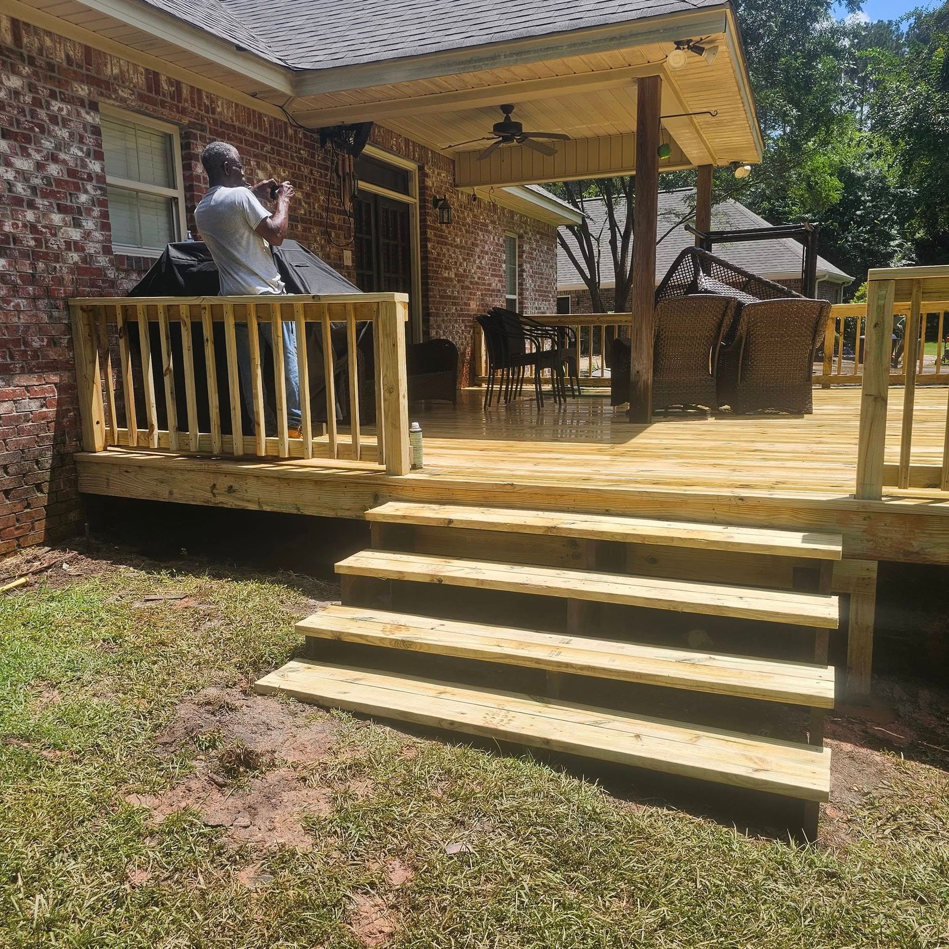 A man is standing on a wooden deck in front of a brick house.