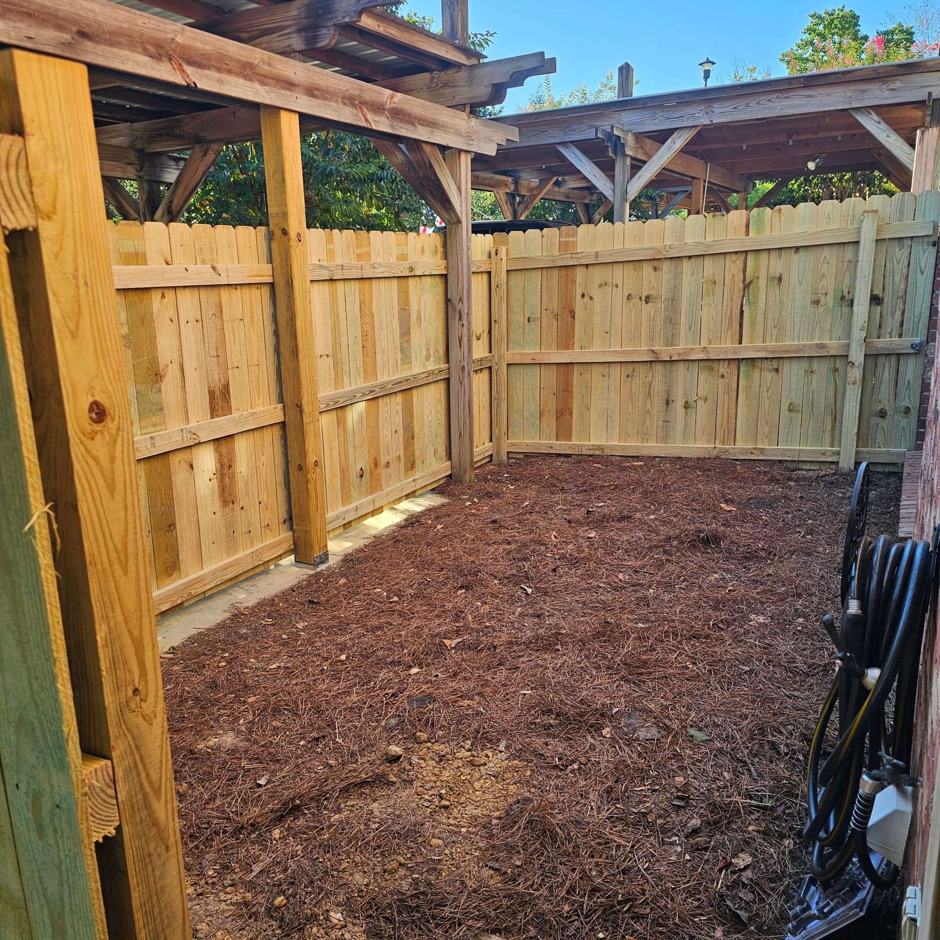 A wooden fence surrounds a pile of mulch in a backyard.