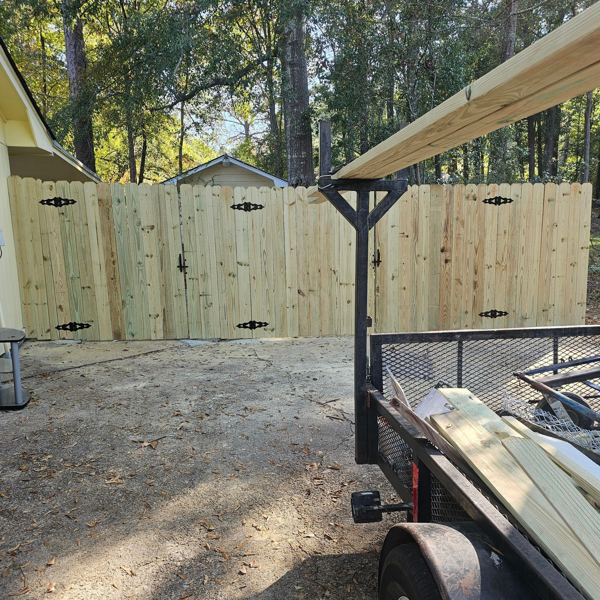A wooden fence is being built next to a trailer filled with wood.