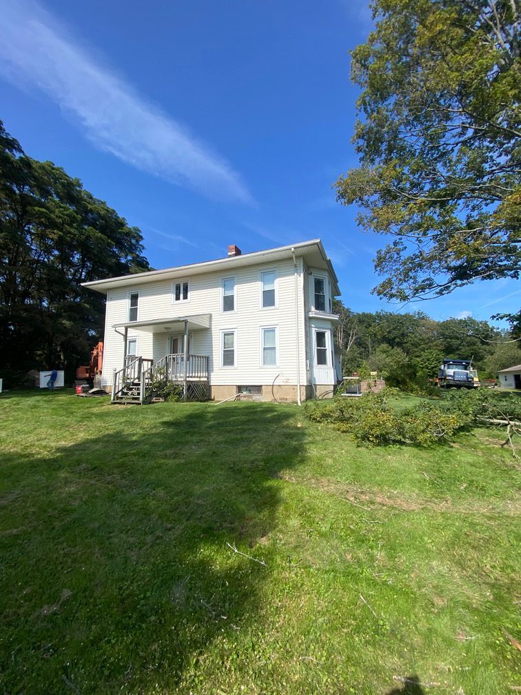 A large white house is sitting in the middle of a lush green field.