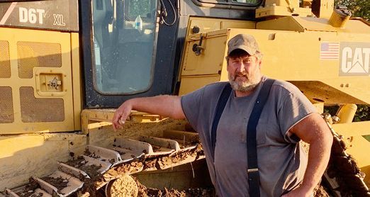 A man standing in front of a yellow cat bulldozer
