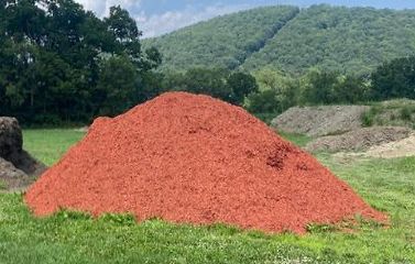 A large pile of red mulch is sitting on top of a lush green field.