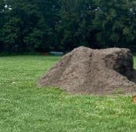 A large pile of dirt is sitting on top of a lush green field.