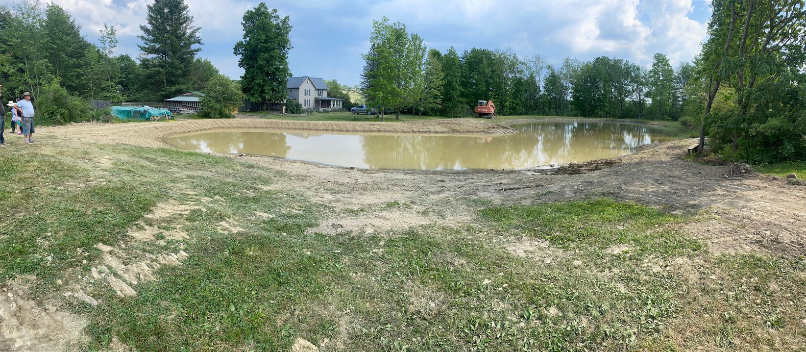 A large body of water [pond building] surrounded by trees and grass in a field.