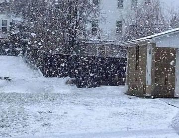 A snowy yard with a garage and a house in the background.