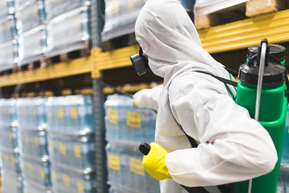 A Man in a Protective Suit is Spraying Chemicals in a Warehouse — Territory Pest Control In Howard Springs, NT