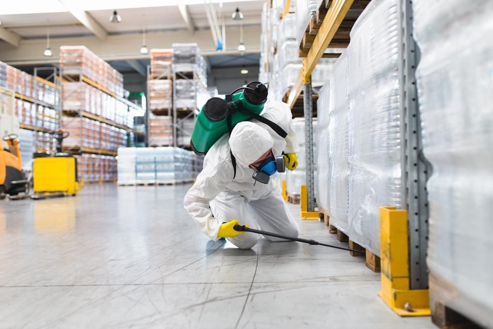 Pest control technician in protective suit spraying warehouse shelves
