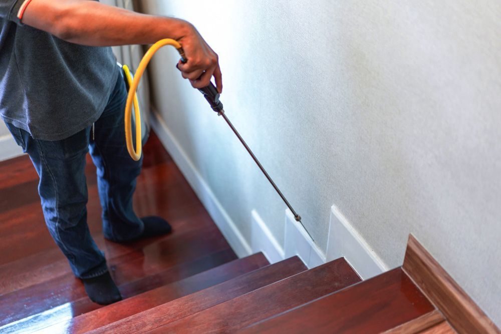 A Man is Spraying a Hose on a Wooden Staircase — Territory Pest Control In Darwin, NT